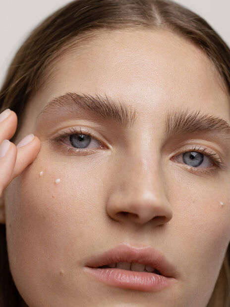 Woman applies eye cream under her eye with ring finger