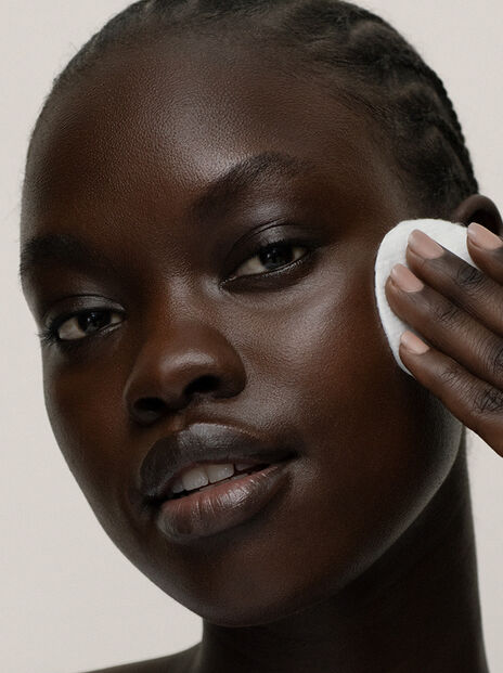 Model wiping her cheekbone with white cotton pad