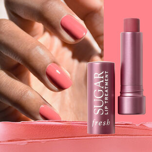 A hand with pink nail polish next to an opened lip treatment case with a smearing of pink lip treatment below.