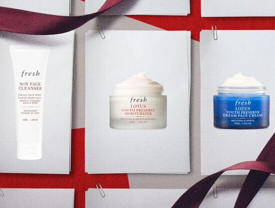 A hand holds Soy Face Cleanser over a blue fresh gift box filled with Kombucha Essence and Tea Elixir