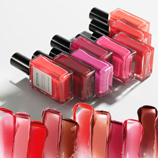 Nail polish bottles in various shades of pinks, reds, and browns, lying against a white background with smears of nail polish in the same shades at the bottom of the image.