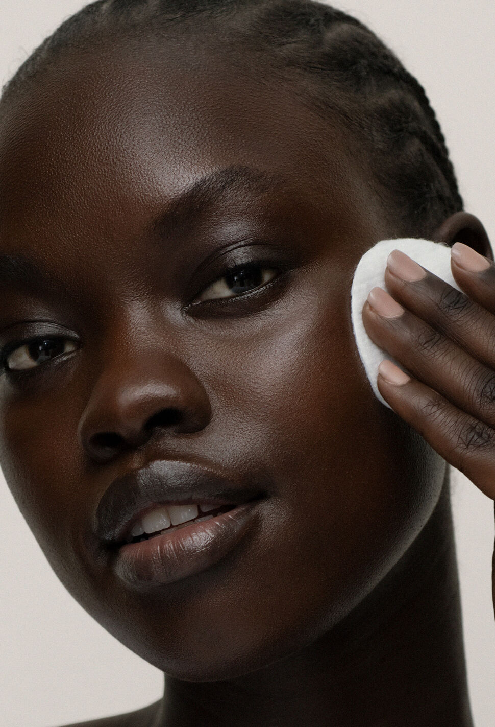 Model wiping her cheekbone with white cotton pad