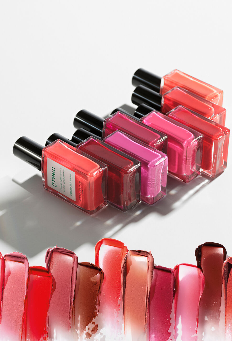 A line of 8 Manucurist nail polish bottles in shades of pink and red lined up on their side