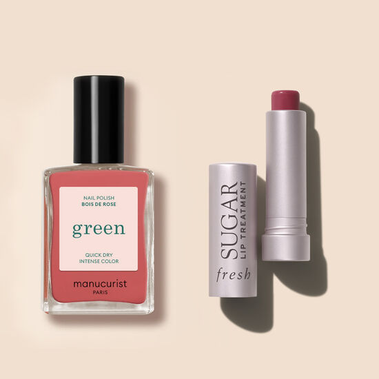 Pink nail polish bottle and opened pink lip treatment case against a peach background.