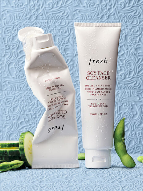 Crumpled and full Soy Face Cleanser tubes with sliced cucumber and soy bean on blue background