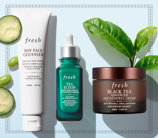 A hand holds Soy Face Cleanser over a blue fresh gift box filled with Kombucha Essence and Tea Elixir