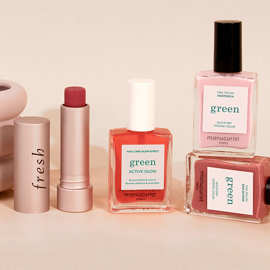 A stack of nail polish in various shades of pink next to an opened lipstick case against a peach background. 