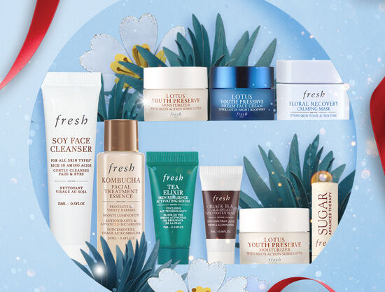 A hand holds Soy Face Cleanser over a blue fresh gift box filled with Kombucha Essence and Tea Elixir