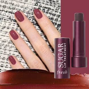 A hand with deep violet nail polish next to an opened lip treatment case with a smearing of mauve lip treatment below.