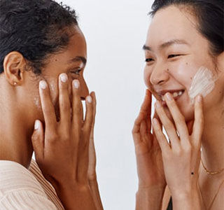 Two women smiling at each other while applying face cream