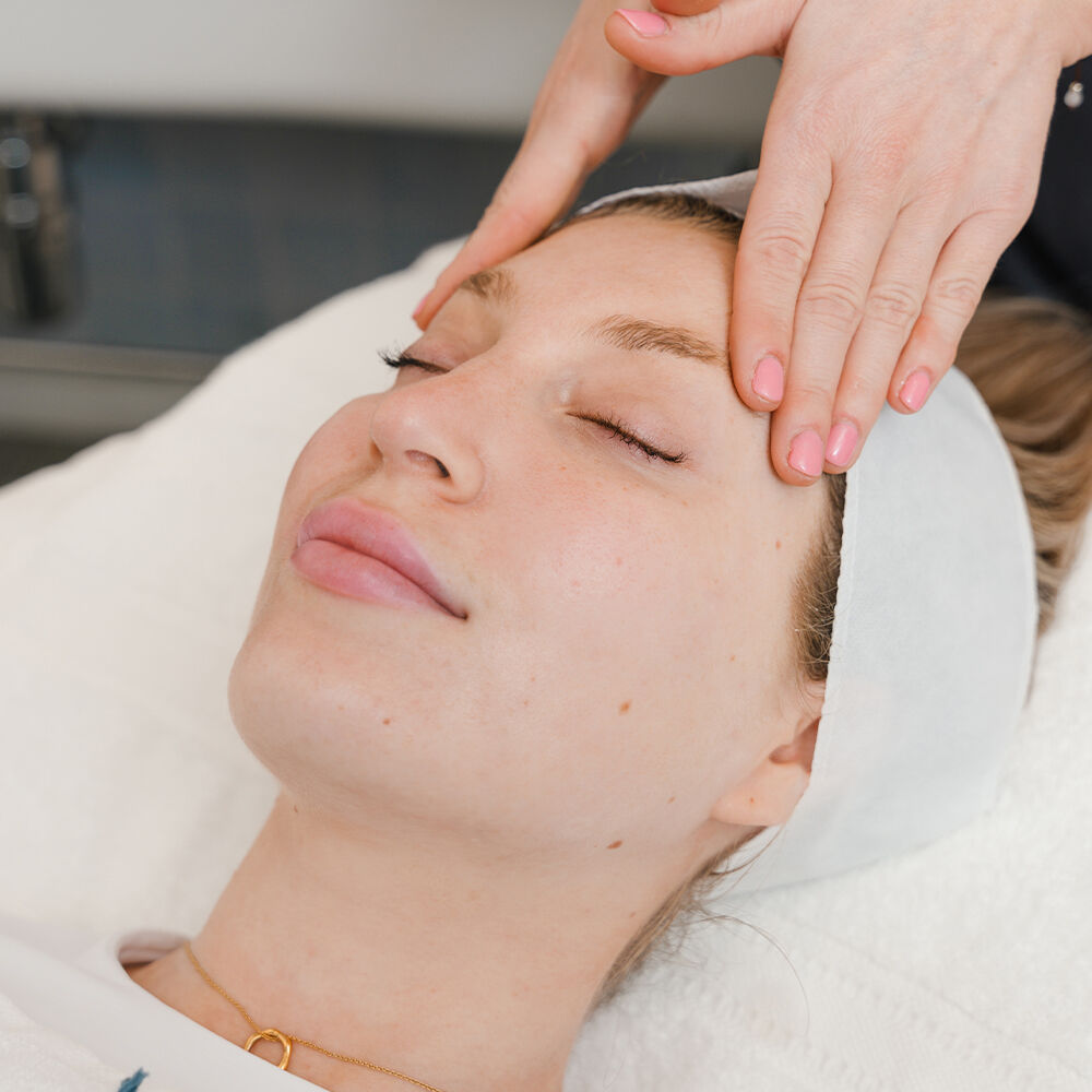 A women lying down with her eyes closed getting her face massaged